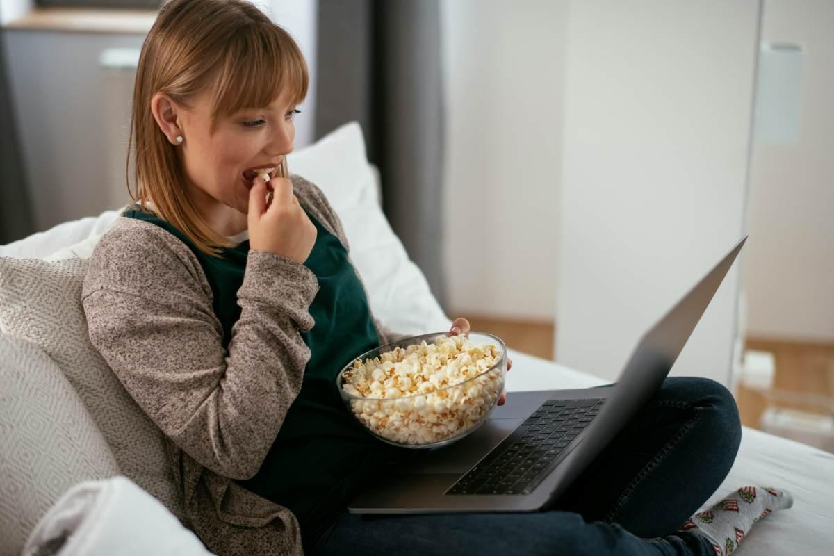 girl streaming on laptop eating popcorn on couch